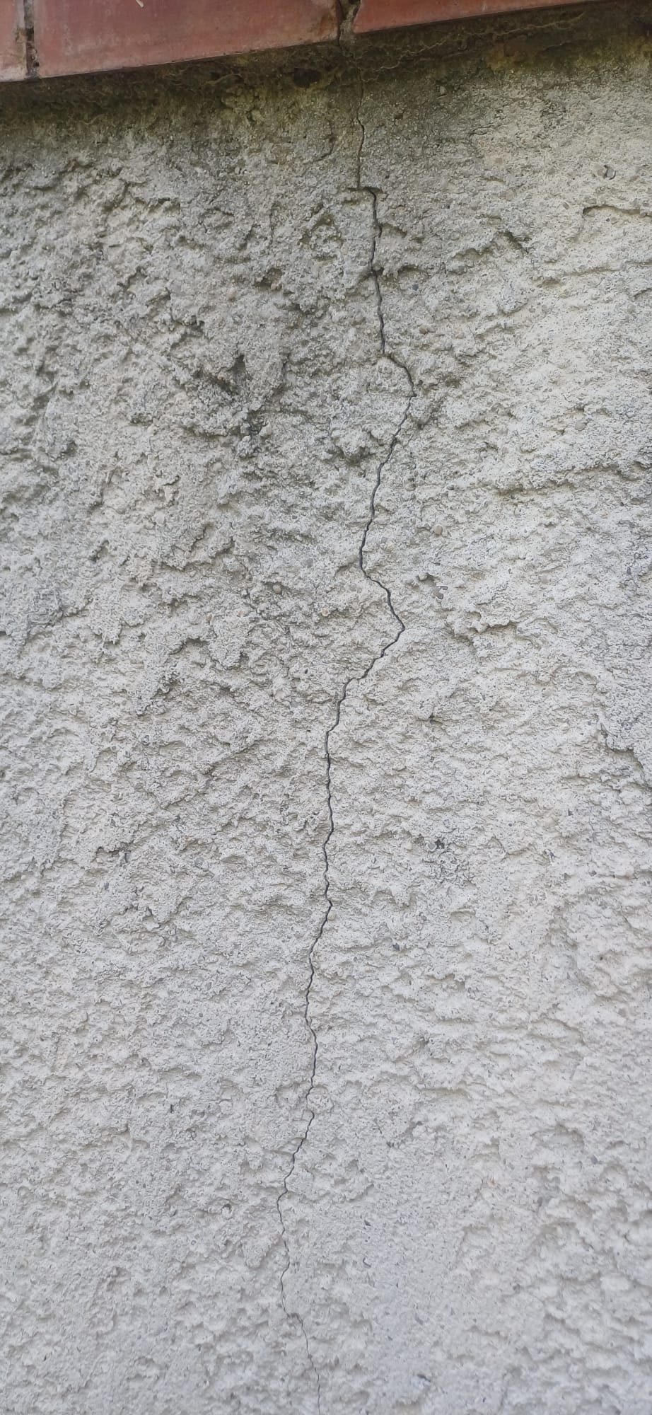 Gros plan d'une fissure traversante sur un mur extérieur en crépi nécessitant une expertise technique.